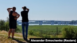 Two men look toward the Antonivskiy Bridge across the Dnieper River in the Russian-controlled Ukrainian city of Kherson after a Ukrainian air strike hit the bridge, forcing authorities to close it on July 27.