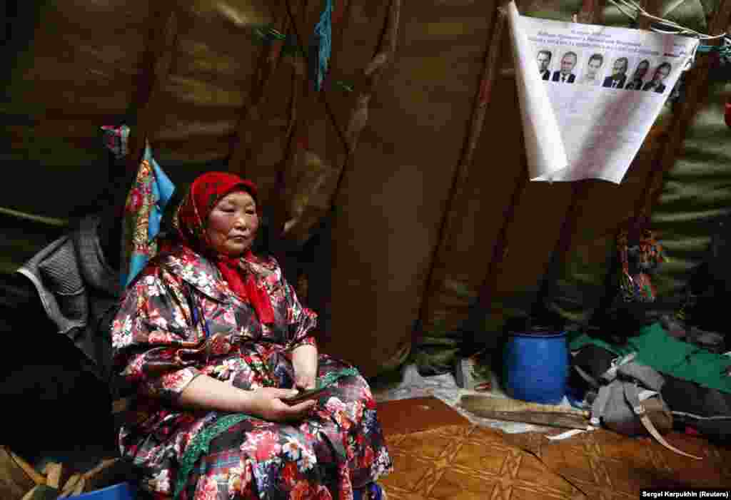 A woman sits under a sheet of paper with information about the presidential candidates, inside a chum - a large tent made of tall wooden poles covered with reindeer hides.